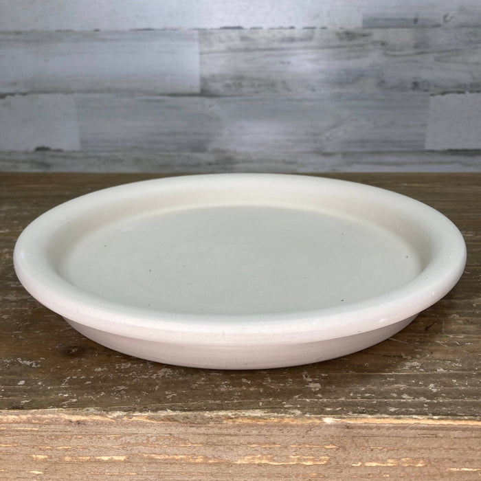 A Saucer - Clay - Granite by Available for Pick-up & Delivery sits on a wooden surface against a light gray textured wall. With slightly raised edges and a smooth finish, it adds understated elegance to any setting, perfectly complementing a 13-inch pot.