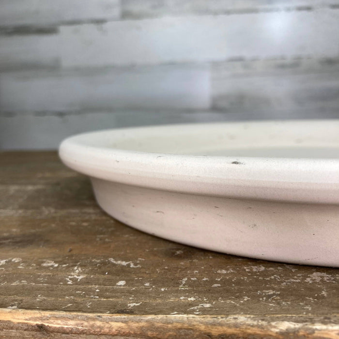 Close-up of a white ceramic Saucer - Clay - Granite by Available for Pick-up & Delivery, resting on a rustic wooden surface. This piece enhances modern decor against the textured gray wall backdrop.