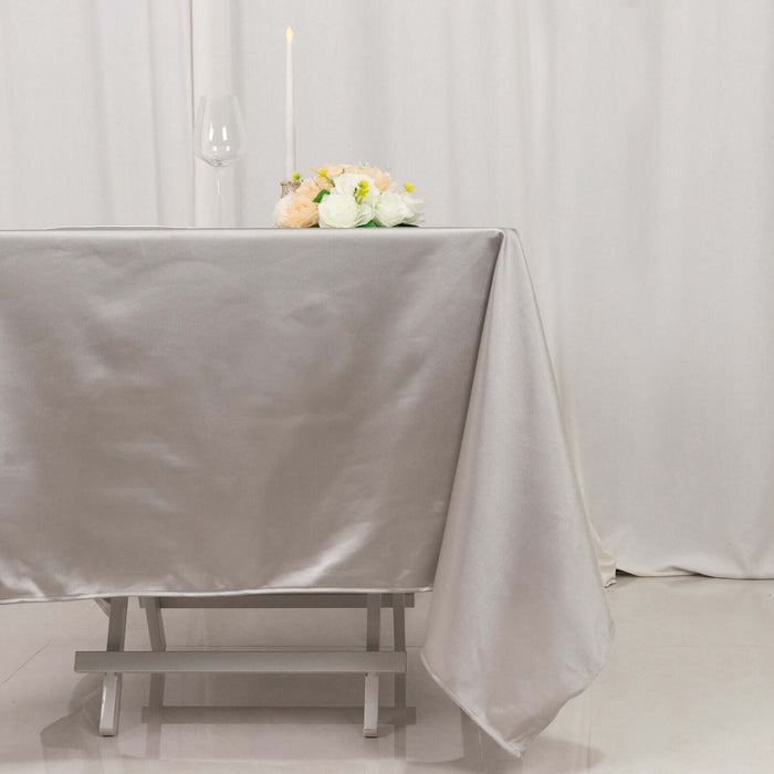 Elegant silver tablecloth draped over a wooden table with flowers and candle.